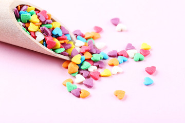 Wall Mural - Colorful heart shaped sprinkles with wooden scoop on pink background