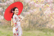 Japanese Girl Wearing A Kimono Holding A Red Umbrella. Beautiful Female Wearing Traditional Japanese Kimono With Cherry Blossom In Spring, Japan. Asian Woman Tourists.