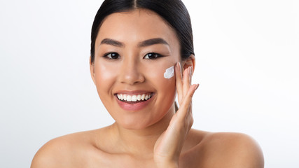 Wall Mural - Morning routine. Asian girl applying cream on cheeks