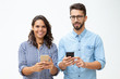 © Mangostar - Cheerful young couple using smartphones. Front view of happy young man and woman holding mobile phones and smiling at camera on white background. Technology concept
