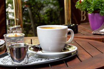 A big white cup of hot chocolate served on a garden table outdoors.