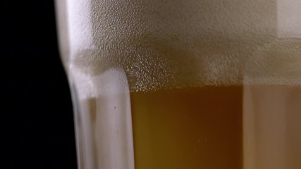 Wall Mural - Close up of fresh and cold craft beer in a glass with white foam on top on black background. Macro shot of flowing foamy wheat or lager beer on dark background