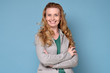 © Viktor Koldunov - Confident attractive blond middle aged woman with folded arms standing in front of a blue wall smiling happily at the camera. Positive facial human emotion.