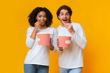 Wall Mural - Young multiracial couple eating popcorn from buckets and looking at camera