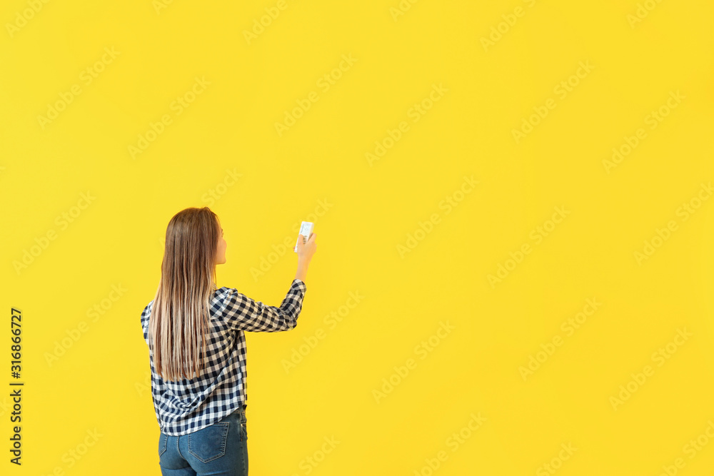 Young woman with air conditioner remote control on color background
