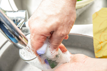 Canvas Print - Washing dishes in the kitchen. The concept of care for the cleanliness of dishes. The man washes the dirty glass by hand. Using a dishwashing sponge and liquid.