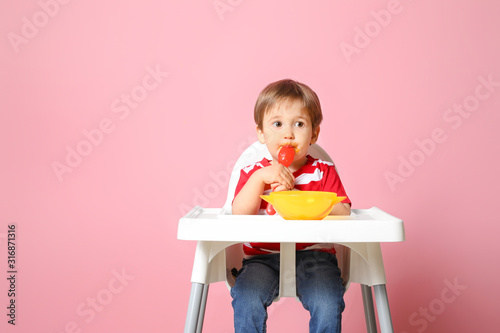 Fotomural Cute little boy eating tasty baby food against color background