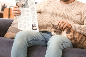 Man with cute cat reading newspaper at home