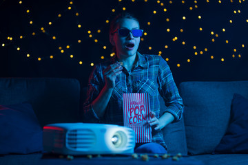 Wall Mural - Home entertainment, watching movies and movies, a girl in 3D glasses with popcorn on a sofa at home watching movies through a projector