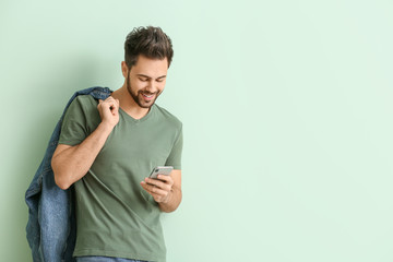 Happy young man with mobile phone on color background