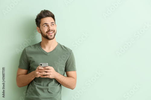 Fotografía Happy young man with mobile phone on color background
