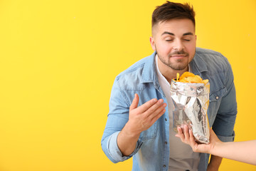 Handsome young man and hand with tasty potato chips on color background