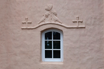 Wall Mural - Fragment of the wall of an old church with a window decorated with a bas-relief in the form of two birds