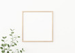 Interior poster mockup with square wooden frame on empty white wall decorated with plant branch with green leaves. 3D rendering, illustration.
