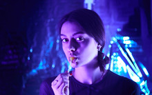 Beautiful Girl With A Lollipop In Her Mouth Cute Looking At Camera. Neon Lamps. Model Posing.    