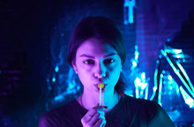 Girl With A Lollipop In Her Mouth Looks Seriously At The Camera. Neon Lamps. Model Posing.