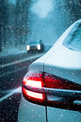 Rear red tail light on white car stopped on road during a snow storm