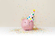 Pink Piggy Bank With Birthday Cap And Color Confetti On Beige Background