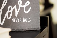 Grey Love Never Fails Sign On A Blurred Background