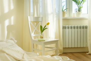 Light spring bedroom interior, bed, white chair, glass with yellow tulip