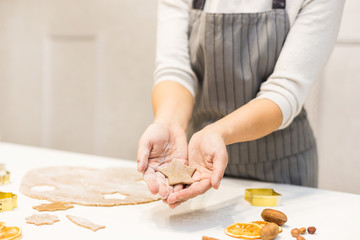 Wall Mural - Young pretty woman prepares the dough and bakes gingerbread and cookies in the kitchen. She holds a star cut from the dough in her hands. Merry Christmas and Happy New Year.