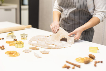 Wall Mural - Young pretty woman prepares the dough and bakes gingerbread and cookies in the kitchen. She makes a star shape on the dough. Merry Christmas and Happy New Year.