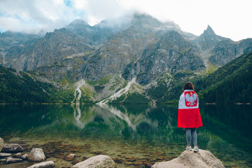 Wall Mural - young woman covered with poland flag looking at lake in tatra mountains