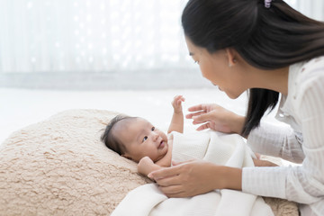asian woman and baby are lying in bed white background. asian mother playing with baby son in bedroo