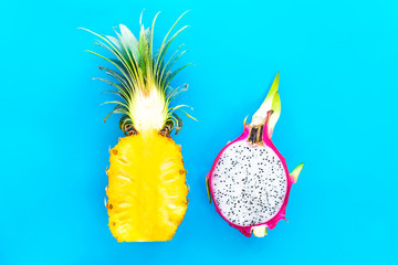 Two 2 halves of ripe yellow pineapple, ananas and dragon fruit, pitaya or pitahaya, cactus. Cut in half exotic tropical fruits isolated on blue background. Top view. Colorful healthy vegan food