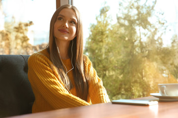 Canvas Print - Woman listening to audiobook at table in cafe