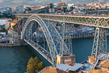 Side View Of The Metalwork Of The Famous Luis I Bridge In The Portuguese City Of Porto Against The Backdrop Of The City And Blue Sky