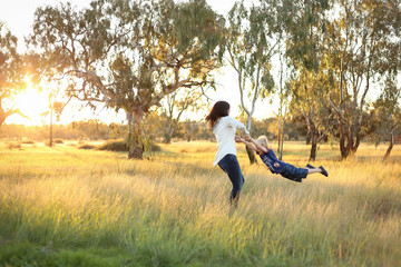 Mother and son playing together in a picturesque field with long grass at sunset. Family time. Mother-son bond. Beautiful image for mother's day with copy space.