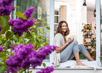 smiling middle-aged woman drinking tea or coffee on the windowsill