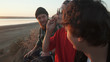 Friends skateboarders smoking joint with weed at seashore at sunset