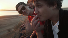 Friends Skateboarders Smoking Joint With Weed At Seashore At Sunset