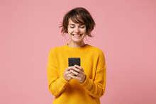 Cheerful Young Brunette Woman Girl In Yellow Sweater Posing Isolated On Pastel Pink Wall Background Studio Portait. People Lifestyle Concept. Mock Up Copy Space. Using Mobile Phone Typing Sms Message.