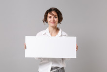 Smiling Pretty Young Business Woman In White Shirt Posing Isolated On Grey Background. Achievement Career Wealth Business Concept. Mock Up Copy Space. Hold White Blank Sign Board With Place For Text.