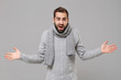 © ViDi Studio - Bewildered young man in gray sweater, scarf posing isolated on grey background, studio portrait. Healthy fashion lifestyle, people emotions, cold season concept. Mock up copy space. Spreading hands.