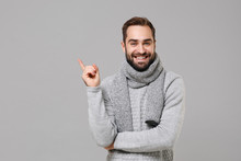 Smiling Young Man In Gray Sweater, Scarf Posing Isolated On Grey Wall Background, Studio Portrait. Healthy Fashion Lifestyle, Cold Season Concept. Mock Up Copy Space. Pointing Index Finger Up Aside.