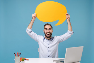 Canvas Print - Funny young man in shirt sit work at desk with pc laptop isolated on pastel blue background. Achievement business career concept. Mock up copy space. Hold yellow empty blank Say cloud speech bubble.