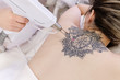 © Rithor - Top view hand of a beautician holds a laser device over a tattooed back of a girl to remove an unwanted tattoo. Concept of erasing tattoos as expensive procedure in beauty parlor modern vedical clinic