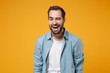 Laughing cheerful young bearded man in casual blue shirt posing isolated on yellow orange wall background, studio portrait. People sincere emotions lifestyle concept. Mock up copy space. Blinking.