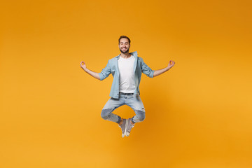 Wall Mural - Smiling young bearded man in casual blue shirt posing isolated on yellow orange wall background. People lifestyle concept. Mock up copy space. Jumping hold hands in yoga gesture, relaxing meditating.
