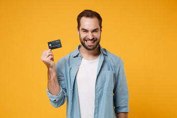 Sticker - Smiling young man in casual blue shirt posing isolated on yellow orange wall background, studio portrait. People sincere emotions lifestyle concept. Mock up copy space. Hold in hand credit bank card.