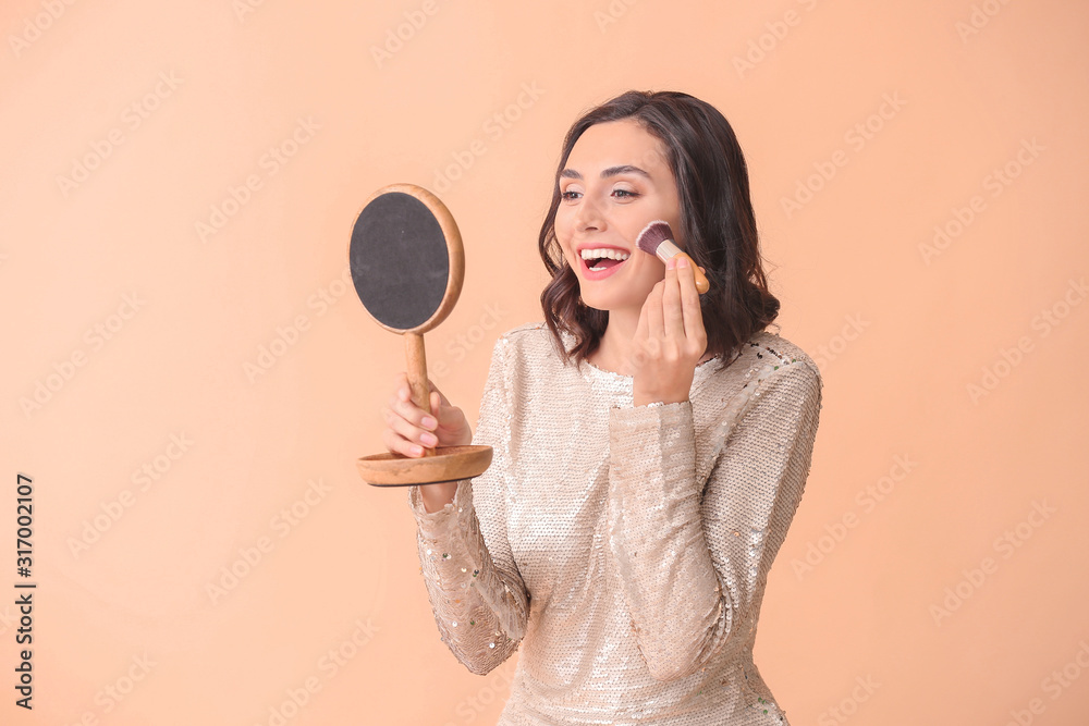Beautiful young woman applying makeup on color background