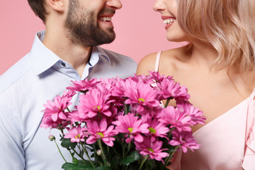 Wall Mural - Cropped image of young couple two guy girl in party outfit celebrating posing isolated on pastel pink wall background. Valentine's Day Women's Day birthday holiday concept. Holding bouquet of flowers.