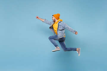 Wall Mural - Side view of young hipster guy in fashion jeans denim clothes posing isolated on pastel blue background. People lifestyle concept. Mock up copy space. Jumping with outstretched hand like Superman.