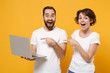 © ViDi Studio - Amazed couple friends bearded guy girl in white blank empty t-shirts isolated on yellow orange background. People lifestyle concept. Mock up copy space. Point index fingers hand on laptop pc computer.