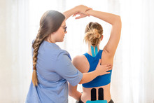 Young Female Patient Wearing Kinesio Tape On Her Back And Neck Exercising With A Professional Physical Therapist. Kinesiology, Physical Therapy, Rehabilitation Concept.