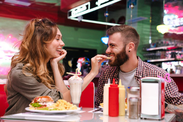 Poster - Loving couple sit in retro bright cafe eat french fries indoors.